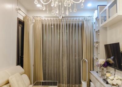 Elegant living room with white chandelier, white sofa, TV, and glass doors