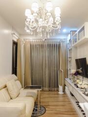 Elegant living room with white chandelier, white sofa, TV, and glass doors