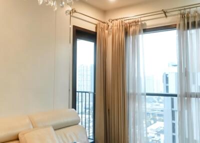 Cozy living room with ceiling chandelier, beige sofa, side table, and large windows with city view