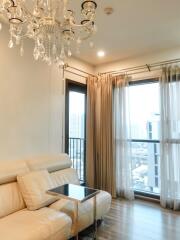 Cozy living room with ceiling chandelier, beige sofa, side table, and large windows with city view