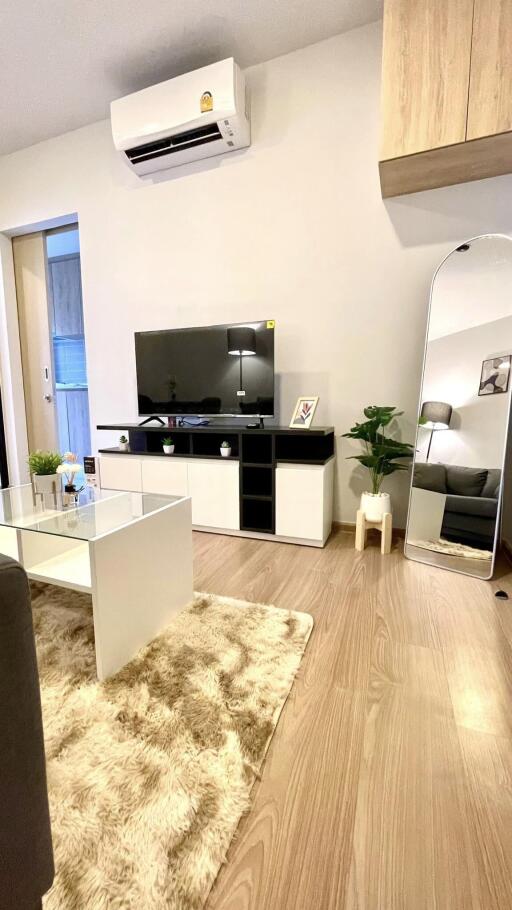 Modern living room with wooden flooring, a flat-screen TV, air conditioning, and decorative elements