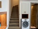 Laundry room with washing machine, stairs, storage cabinet, and door