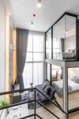 Modern, multi-level living area in a loft-style apartment with a view of the bedroom through glass walls.