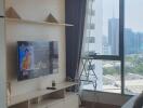 Living room with a TV, shelf, window, and city view