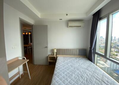 Bedroom with large windows, a bed, a small nightstand, and a city view.