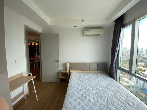 Bedroom with large windows, a bed, a small nightstand, and a city view.