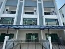 Front view of a modern multi-story residential building with balconies and a gated driveway