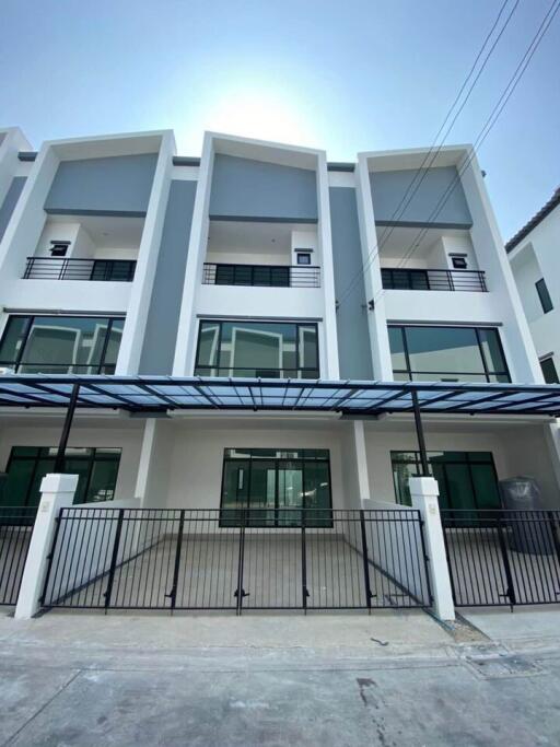 Front view of a modern multi-story residential building with balconies and a gated driveway