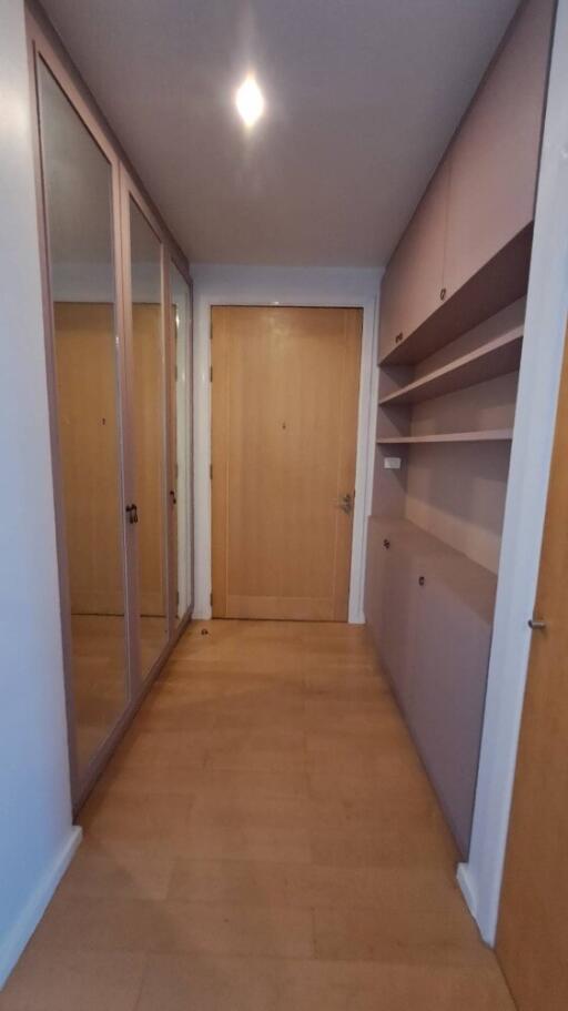 Corridor with wooden flooring, mirrored wardrobe, shelves, and wooden doors