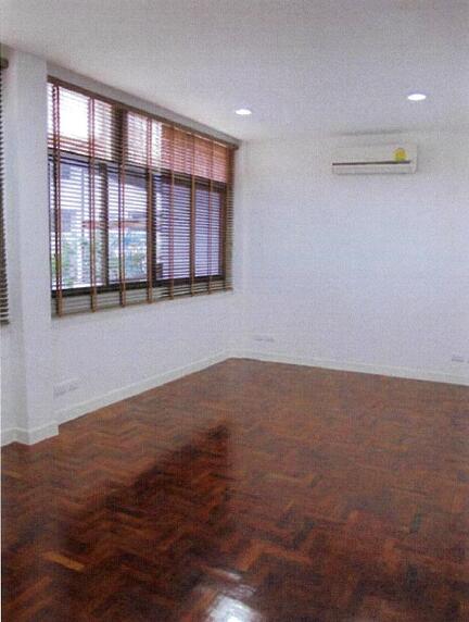 A bright, empty living room with wooden flooring, large windows with blinds, and an air conditioning unit.