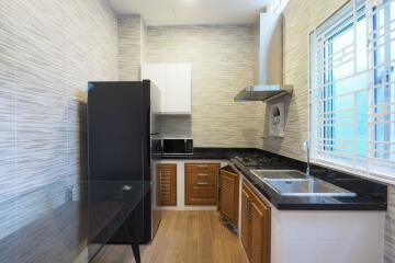 Modern kitchen with black fridge, wooden cabinets, and stainless steel sink