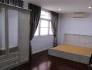 Spacious and well-lit bedroom with wooden flooring, a large wardrobe, and an air conditioning unit