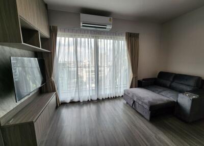 Modern living room with couch, air conditioner, television, and large window with sheer curtains