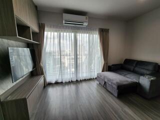 Modern living room with couch, air conditioner, television, and large window with sheer curtains