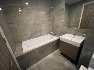 Modern bathroom with tiled walls and floor, featuring a bathtub and a sink.