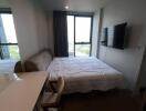 Bedroom with a large window, bed, mounted TV, desk, and chair