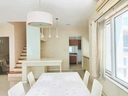 Modern dining area with a table and chairs, adjacent to stairs and a kitchen