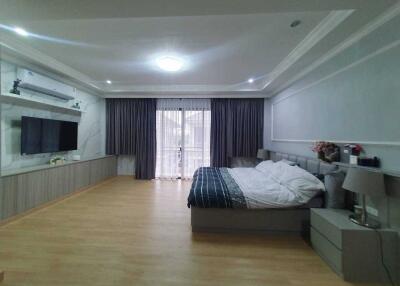 Spacious modern bedroom with large bed, mounted TV, and ample natural light
