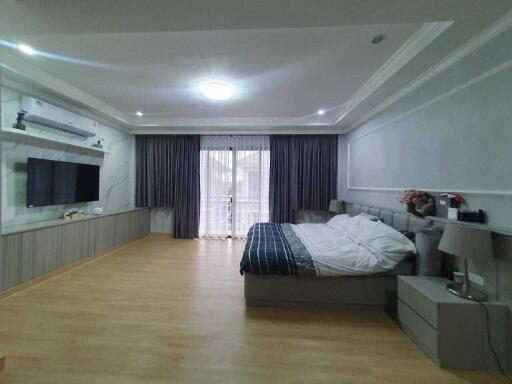 Spacious modern bedroom with large bed, mounted TV, and ample natural light