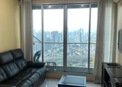 Living room with a black leather sofa, coffee table, TV, and large windows offering city view