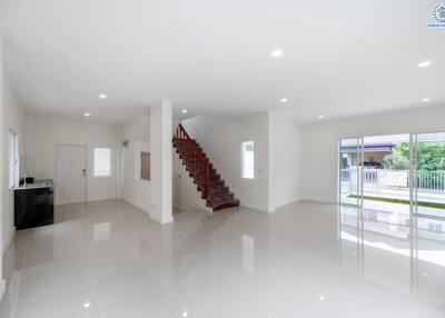 Spacious and well-lit living room with large windows, staircase, and glossy tiled floors