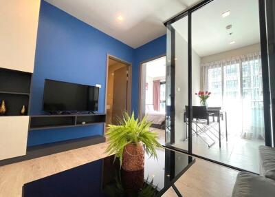 Modern living room with blue accent wall, wall-mounted TV, and glass partition leading to a dining area.