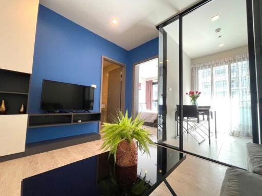 Modern living room with blue accent wall, wall-mounted TV, and glass partition leading to a dining area.