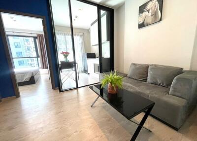 Modern living room with a sofa, coffee table, and a view of an adjacent bedroom and kitchen