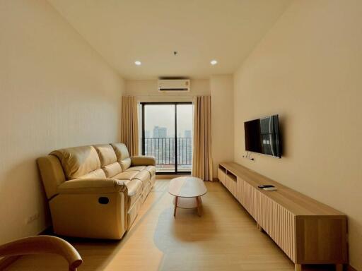 Modern living room with sofa, wall-mounted TV, and large window