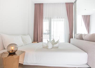 Modern bedroom with white bedding, bedside table and lamp, with a large window and pink curtains