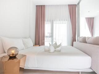 Modern bedroom with white bedding, bedside table and lamp, with a large window and pink curtains