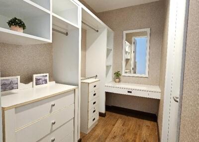 Spacious walk-in closet with wooden flooring, white shelving, and a vanity table