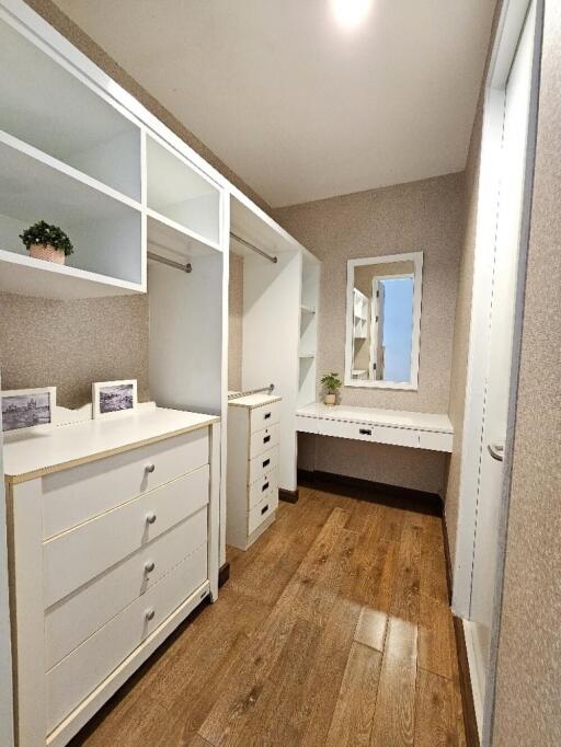 Spacious walk-in closet with wooden flooring, white shelving, and a vanity table