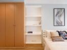 Modern bedroom with wooden wardrobe, bed with pillows and wall art.