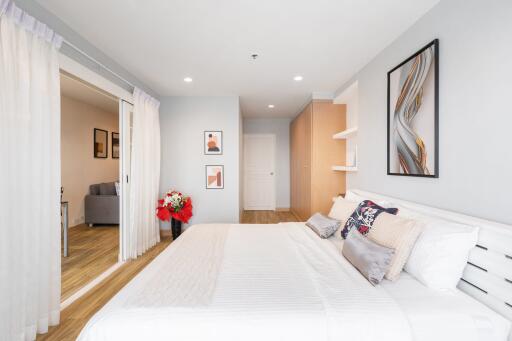 Modern bedroom with white bedding, minimalistic art, and a view leading to a living room