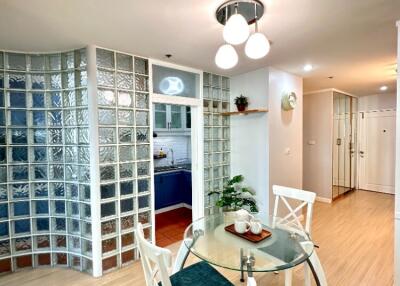 Modern dining area with a glass table and chairs, adjacent to the kitchen with glass block wall partition