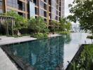 Modern high-rise building with a reflective swimming pool and surrounding greenery.