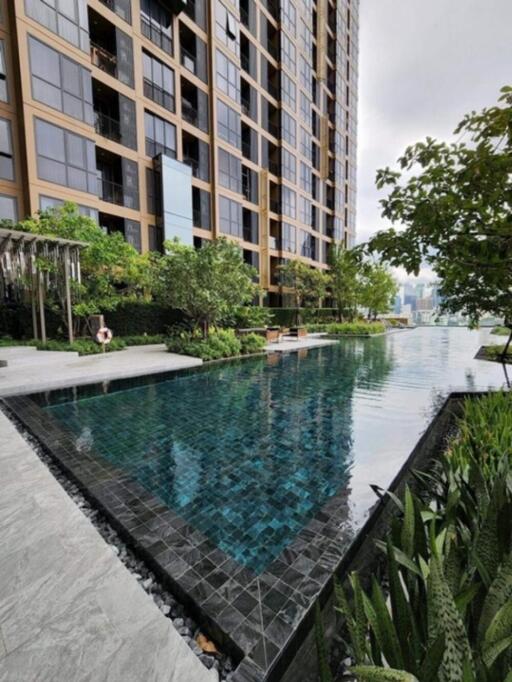 Modern high-rise building with a reflective swimming pool and surrounding greenery.