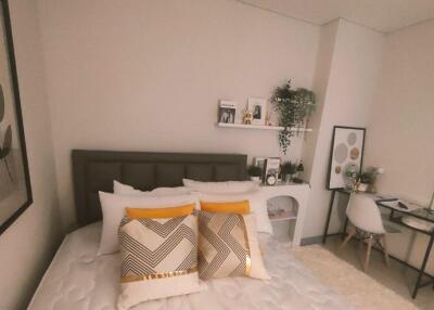 Cozy bedroom with bed, cushions, wall art, shelves, desk, and chair