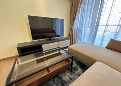 Modern living room with a glass coffee table, flat-screen TV, and large window with drapes