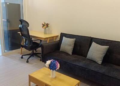 Modern living room with a black sofa, wooden coffee table, desk with office chair, and a sliding glass door