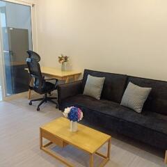 Modern living room with a black sofa, wooden coffee table, desk with office chair, and a sliding glass door