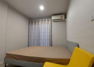 Modern bedroom with a large bed, bright yellow chair, air conditioner, curtain-covered window, and ceiling light