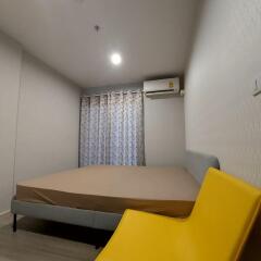 Modern bedroom with a large bed, bright yellow chair, air conditioner, curtain-covered window, and ceiling light