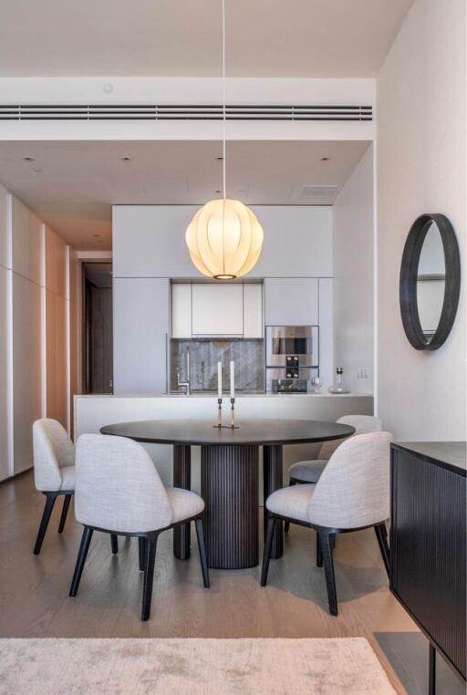 Modern dining area with round table, four chairs, elegant light fixture, and a view into a minimalist kitchen.