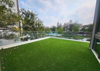 Spacious balcony with artificial grass and glass railing, overlooking garden