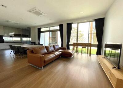 Modern living room with brown leather sofa, large windows, dining area, and flat-screen TV