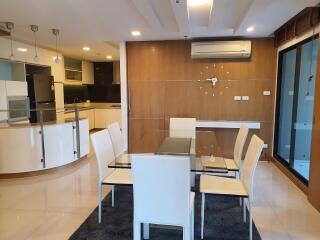 Modern dining area with glass table and white chairs, open kitchen in the background