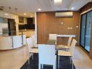 Modern dining area with glass table and white chairs, open kitchen in the background