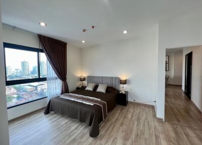 Spacious bedroom with large window offering city view, modern furnishings, and wood flooring.